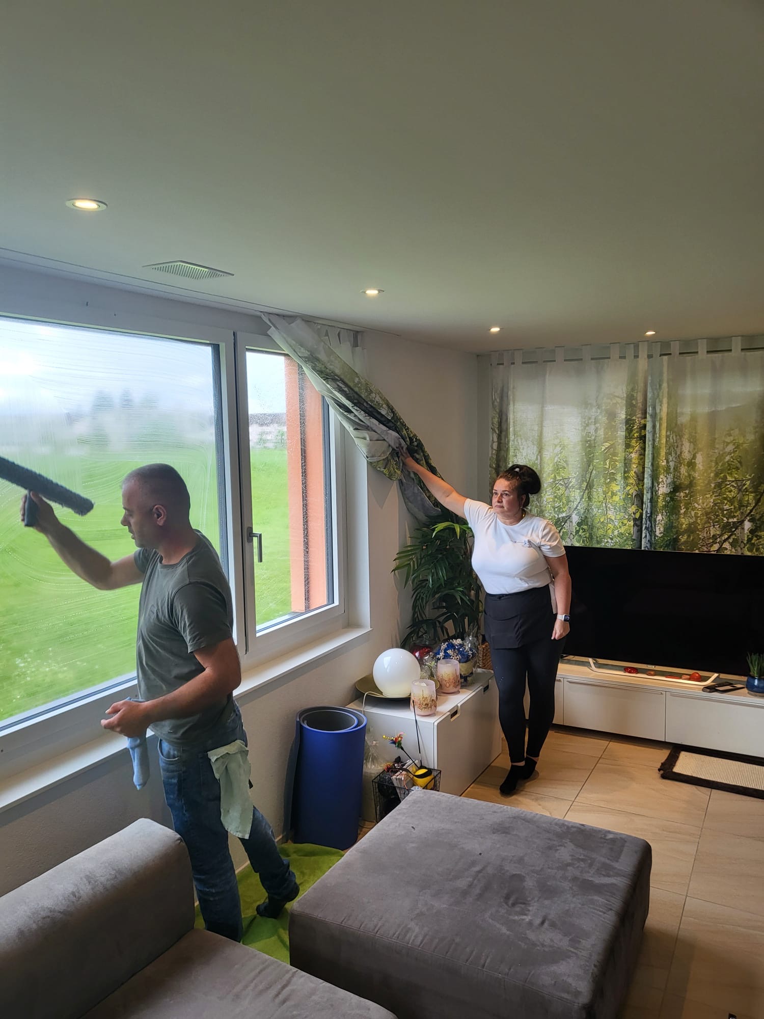 Zwei Mitarbeitende reinigen ein Wohnzimmer mit Fensterfront